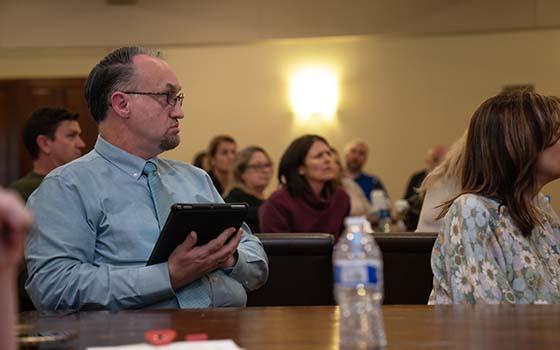 faculty members listening with attendee in foreground holding i-pad