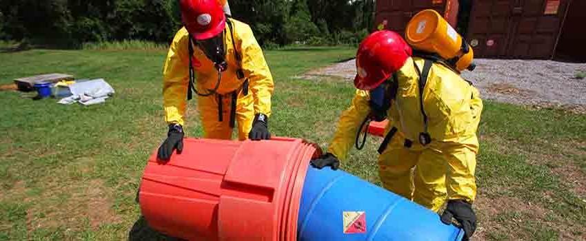 Two men in hazmat suits handling container