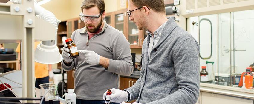 Two males looking at bottle in chemical engineering lab.