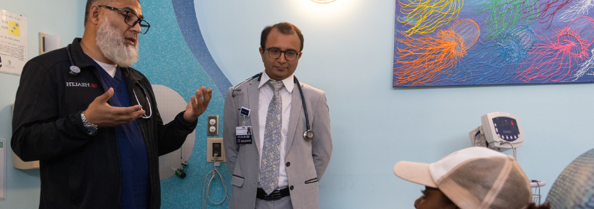 Two physicians speak with a female pediatric patient receiving treatment.