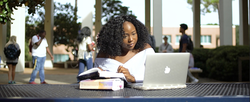 Female studying laptop outside of Humanities building.