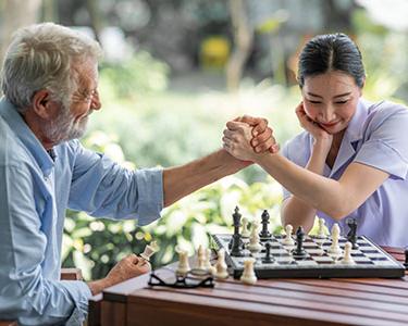 A younger woman and older man playing chess outside.