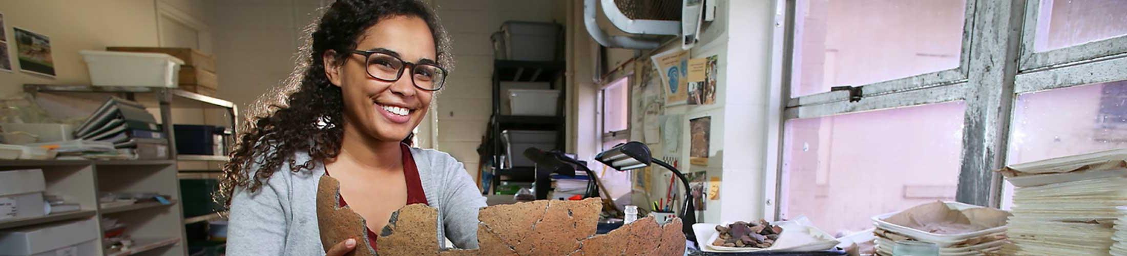 Female student holding an artifact in a lab.