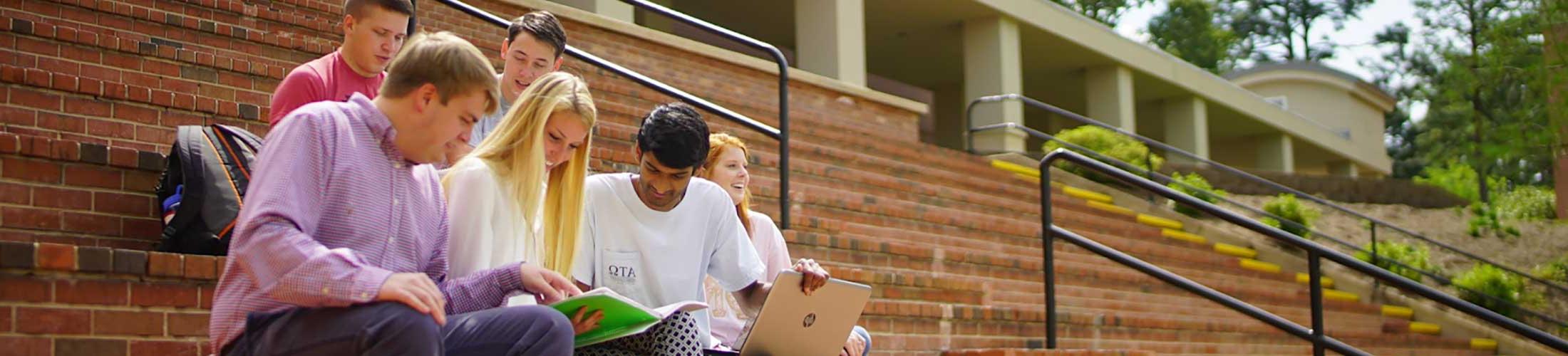 Group of students studying sitting on stairs on campus.