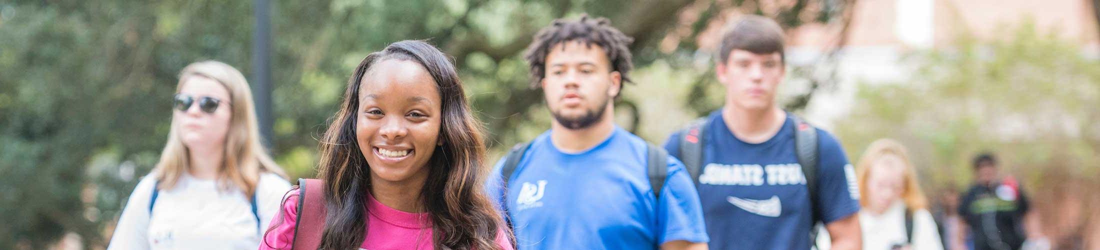 Female student walking on campus smiling.