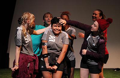 Students in soccer uniforms performing a play.