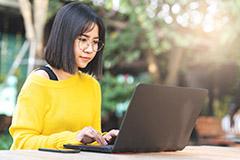 Woman sitting and working on laptop outside.