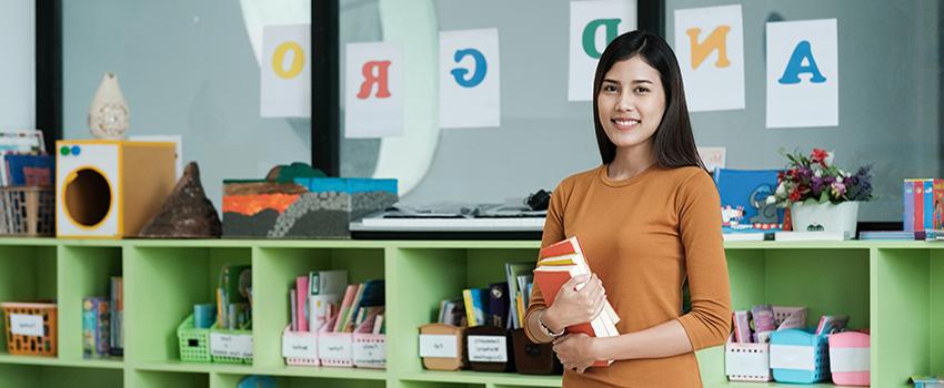 Teacher holding books in classroom.