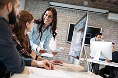 Woman smiling holding papers in front of two people working on a computer.