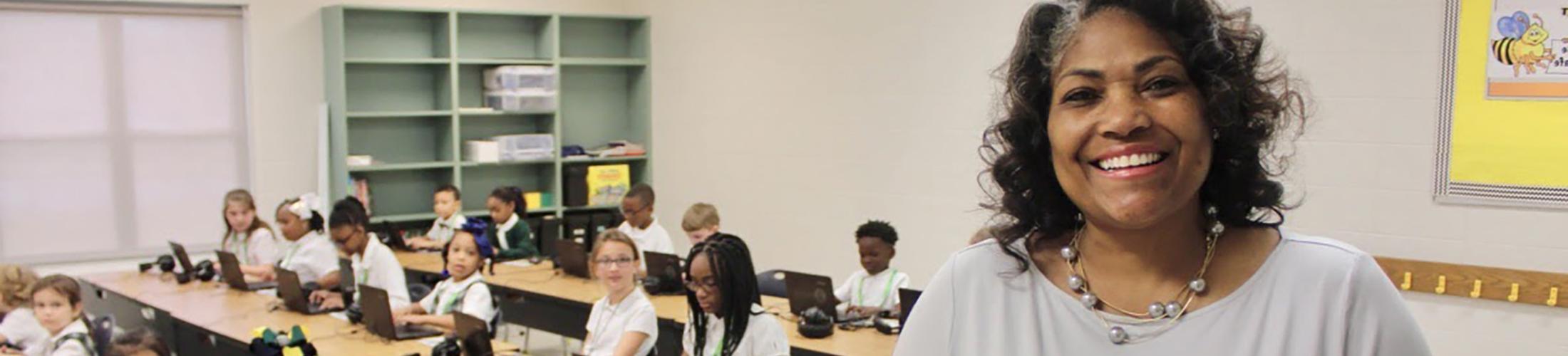 Teacher smiling in front of class of kids.