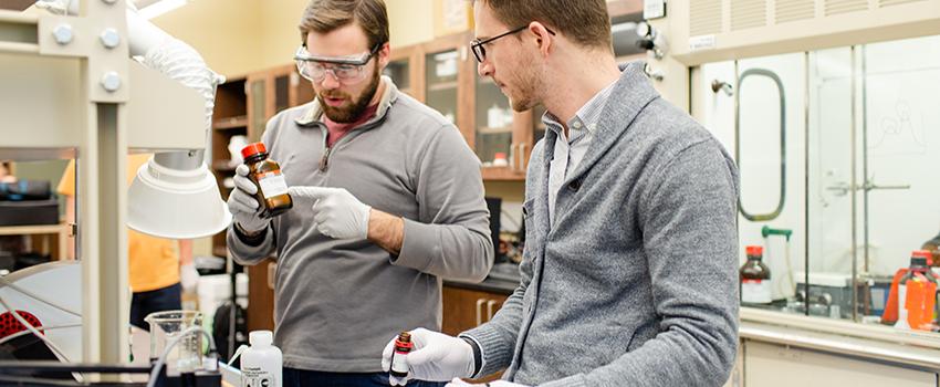 Two male students looking at bottle in lab.