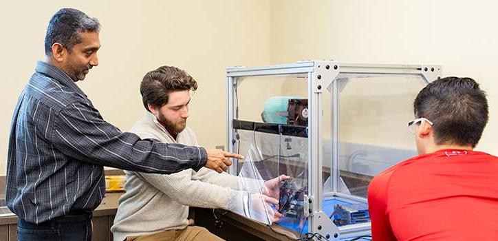 Electric Engineering students working on a machine with professor.