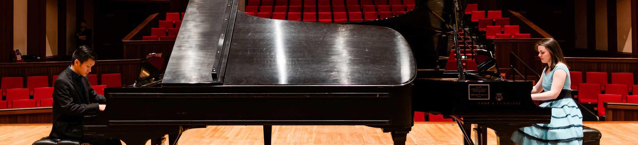 Two students playing piano on stage.