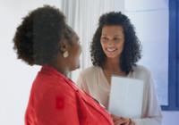 Two people smiling and talking holding a clipboard.