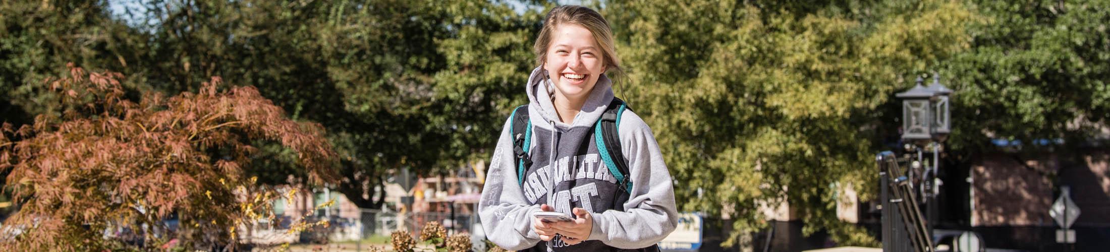 Female student smiling wearing backpack walking on campus.