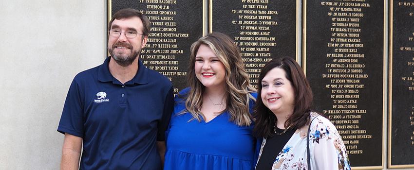 Three alumni in front of Alumni Wall of Donors.