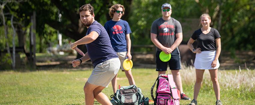 Students playing disc golf on campus with club sports.