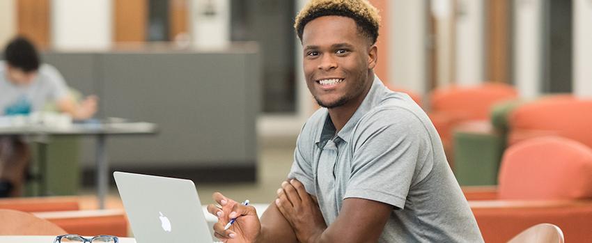 Male student sitting at desk working on a laptop.