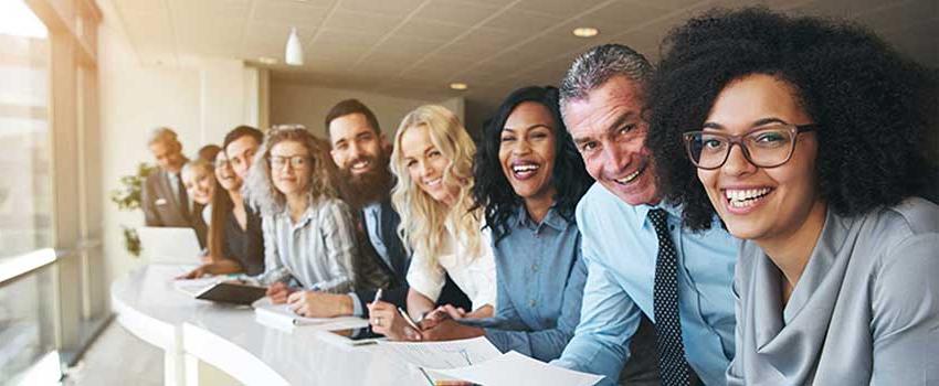 A group of people smiling leaning on counter taking notes.