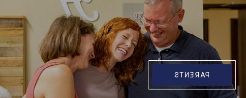 Parents hugging their daughter and laughing in dorm room.