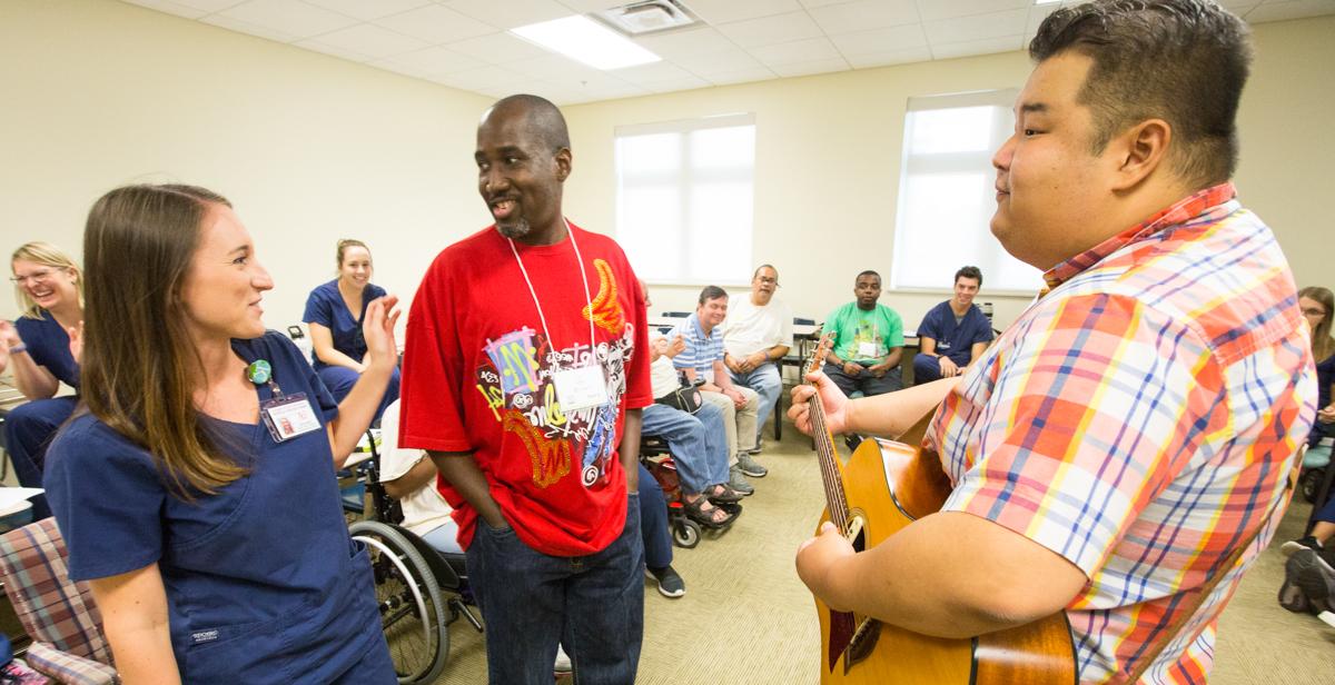 Kelsey Gross, University of South Alabama speech-language pathology graduate student, assists traumatic brain injury camp participant Larry Malone Jr., center, while music therapist Fred Ra leads Malone and other camp participants in creating a song using words suggested by the group.