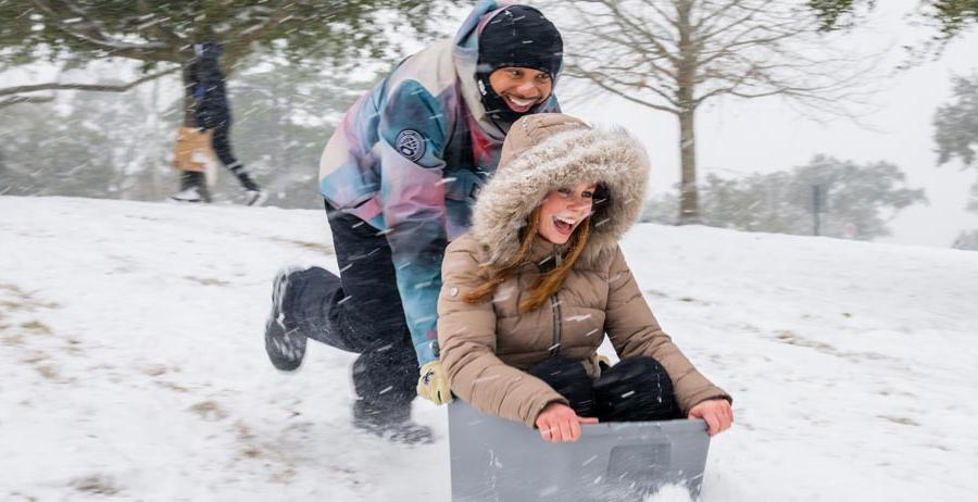 A student is pushed by another sledding down a hill in the snow. 