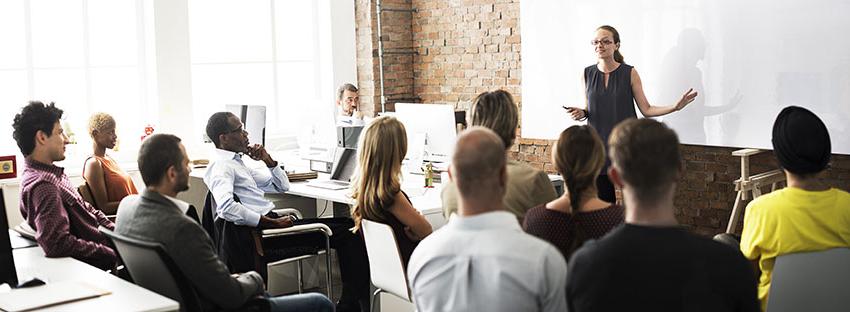 Woman teaching at white board in front of a group of people.